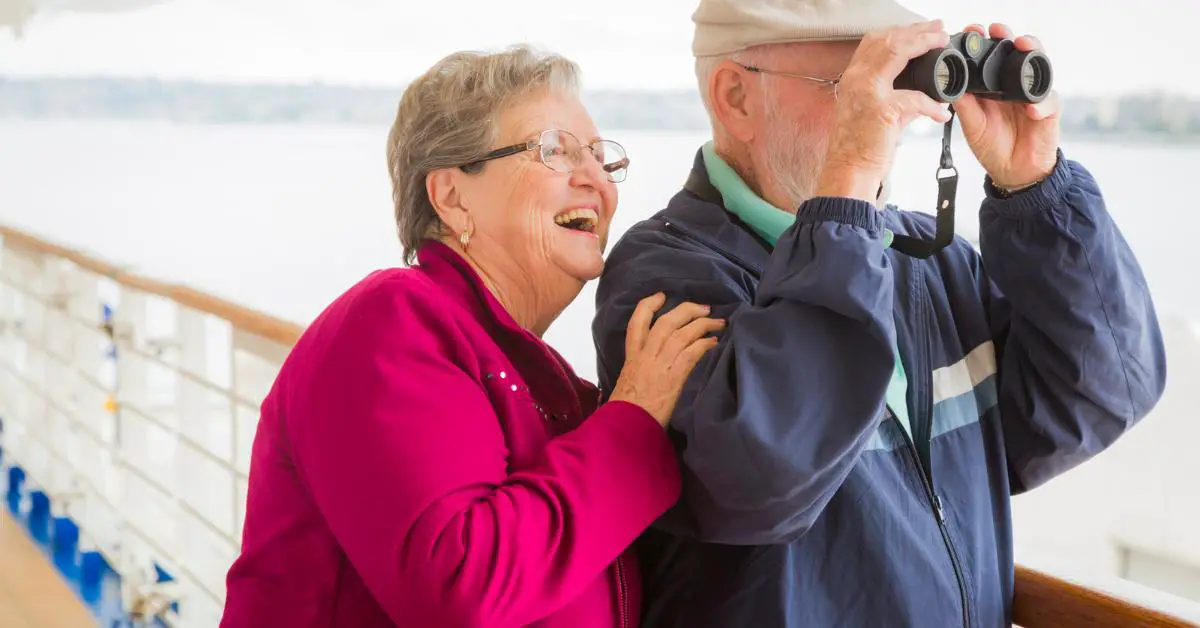 Senior couple over 60 looking through binoculars from deck of cruise ship